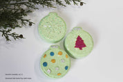 Three green ornament-shaped bath bombs with decorative elements on a white surface with greenery. by Vermont Lavender